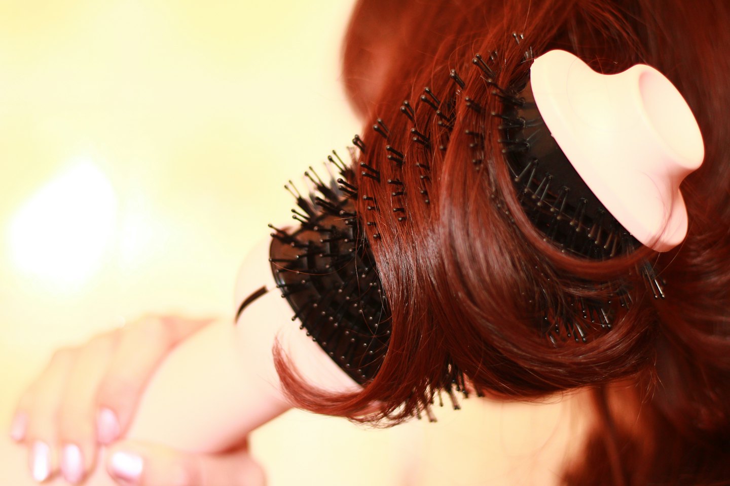 Person styling their reddish-brown hair with a round brush.